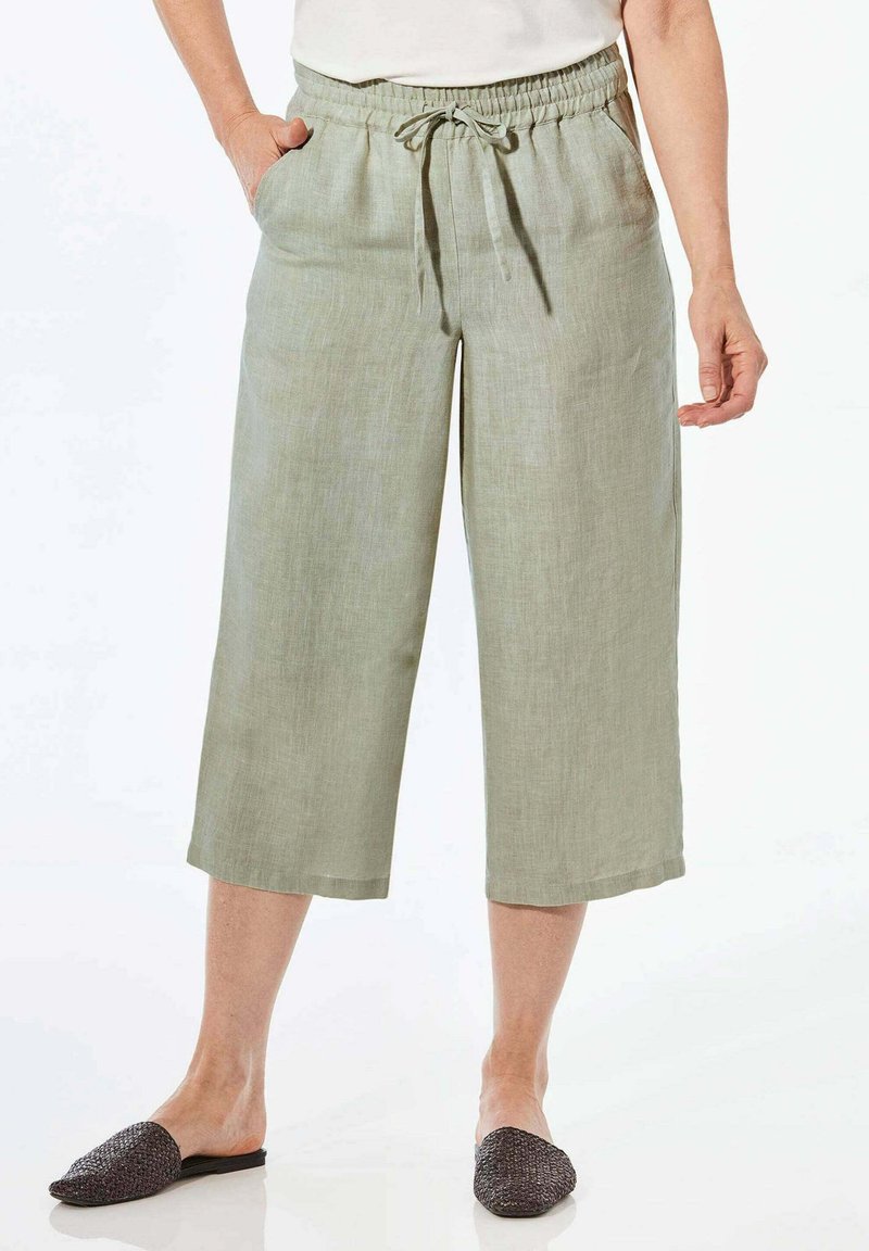 Helle grüne Leinen-Culottes mit einem elastischen Bund, Kordelzug und seitlichen Taschen, die knapp unter dem Knie enden. Flache, strukturierte schwarze Slipper.