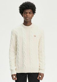 Maglione lavorato a maglia grosso in bianco sporco, collo rotondo, polsini e orlo a coste. Presenta un piccolo logo ricamato sul petto.