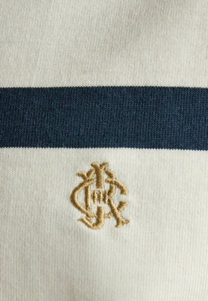 Flødefarvet strikstof med en enkelt mørkeblå vandret stribe og et lille beige broderet monogram under striben.