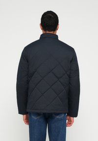 Casaco acolchoado azul-marinho com gola alta, apresentando um acabamento texturizado e padrão em diamante, combinado com jeans azul claro.