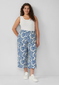 Witte tanktop gecombineerd met een broek met wijde pijpen met een blauw-wit bladerenpatroon. De outfit wordt compleet gemaakt met witte sneakers.