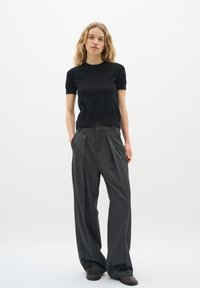 Suéter negro de manga corta con cuello redondo combinado con pantalones gris plisados de cintura alta. Textura suave, diseño de pierna ancha y acentos clásicos.
