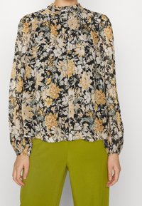 Lätt svart blus med ett blommönster i gult och vitt, med hög hals, veck och långa ärmar med elastiska manschetter.