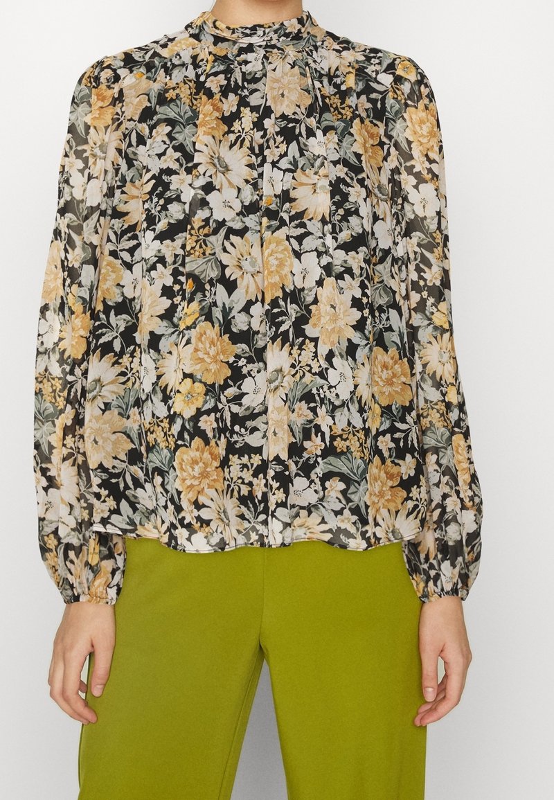 Lätt svart blus med ett blommönster i gult och vitt, med hög hals, veck och långa ärmar med elastiska manschetter.