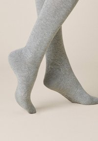Graue Stricksocken mit einer glatten Textur, nahtlosem Design und einem leicht gerippten Saum, der den Unterschenkel bedeckt.