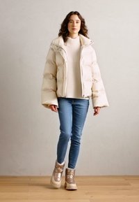 Doudoune blanche avec des manches oversize, pull blanc côtelé, jeans bleu clair et bottines beige avec des accents métalliques.