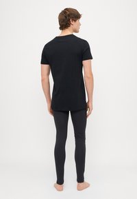 T-shirt en coton noir à manches courtes et col rond, associé à un legging noir, mettant en valeur une coupe slim et une texture lisse.
