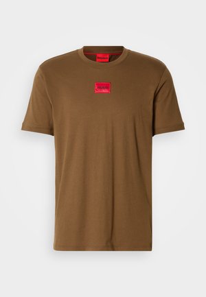 T-shirt marron à manches courtes avec un patch rectangulaire rouge portant l'inscription "HUGO" au centre de la poitrine.