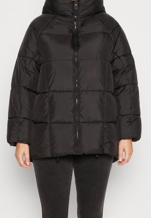 Czarna pikowana kurtka z kapturem i zamkiem z przodu, noszona przez osobę z luźno opartymi rękami wzdłuż ciała, zestawiona z ciemnymi spodniami.