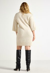 Strikket sweaterkjole i lys beige med ribbet kant og ærmer. Kombineret med knælange sorte læderstøvler med hæl.