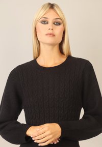 Sort strikket sweater med et kabelmønster på forsiden, ribbede ærmer og rund hals. Blødt, tekstureret stof.