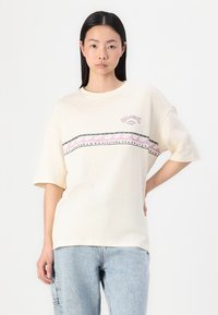 Kreemikaalune oversized T-särk, mis on valmistatud pehmest puuvillast, millel on rinnal värvikas laine- ja kolmnurkade muster ning logo.