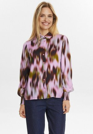 Blusa a maniche lunghe di colore rosa chiaro con motivi astratti marrone scuro e verdi. Presenta un colletto e bottoni sulla parte anteriore. Polsini strutturati.