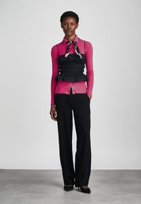 Φούξια μπλουζάκι με μακριά μανίκια, στοιχισμένο πάνω από μια μαύρη ριχτή πετσέτα με λεπτομέρεια από μαντήλι, συνδυασμένο με κομψά μαύρα παντελόνια και μαύρες μπαλαρίνες.