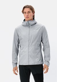 Veste imperméable gris clair avec une fermeture éclair à l'avant, capuche ajustable et poches latérales. Présente une texture lisse et un branding discret.