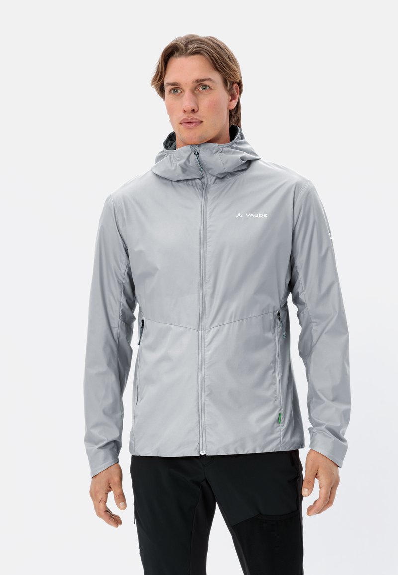 Veste imperméable gris clair avec une fermeture éclair à l'avant, capuche ajustable et poches latérales. Présente une texture lisse et un branding discret.