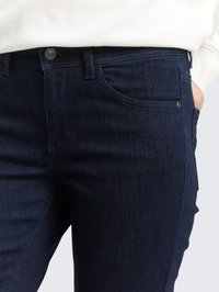 Close-up de uma pessoa a usar jeans de ganga azul escuro, com a mão no bolso e uma camisa branca metida dentro.