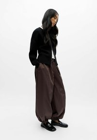 Cardigan noir, chemise blanche et pantalon large marron foncé avec ourlets aux chevilles ; des mocassins noirs complètent l'ensemble. Design simple et moderne.