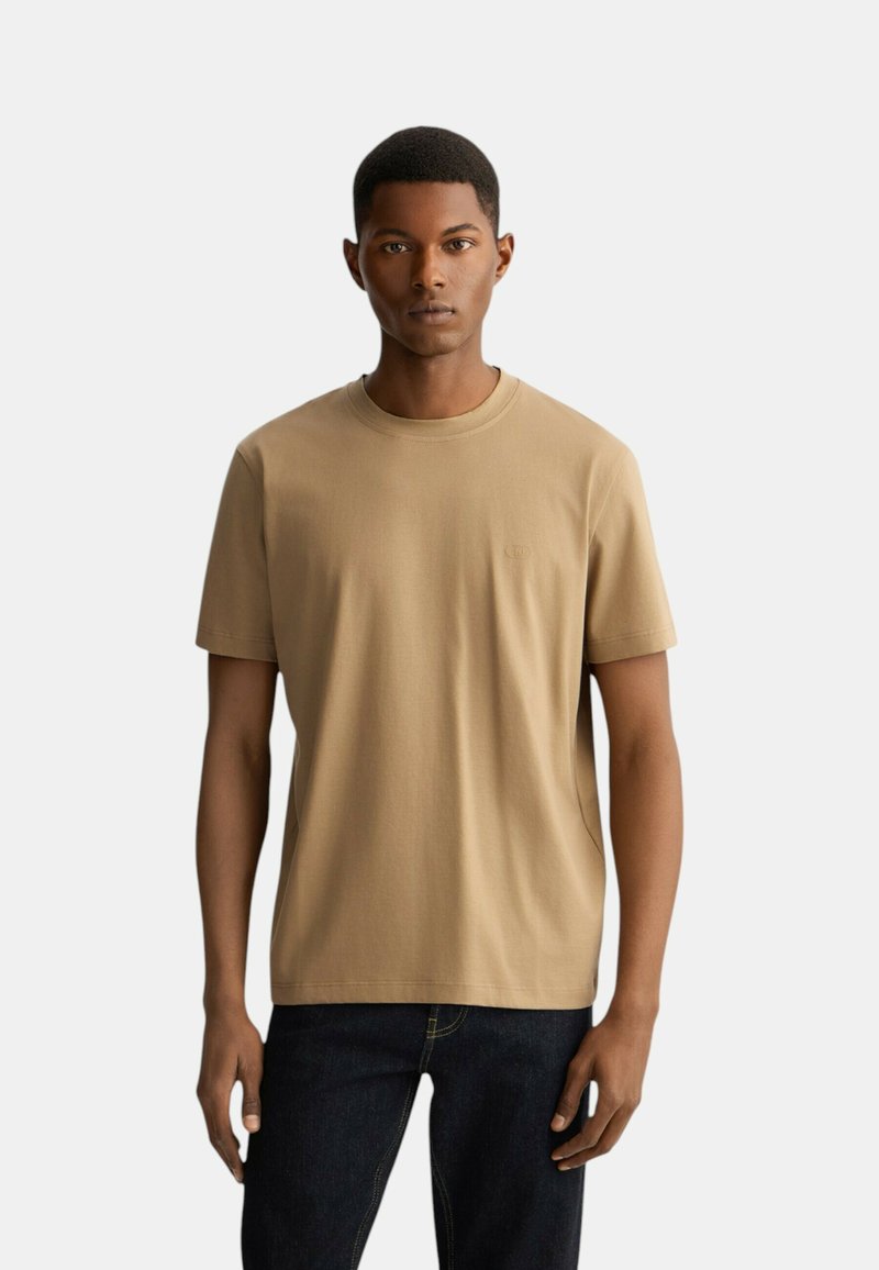 T-shirt in cotone color sabbia con collo a giro e maniche corte. Design semplice con un piccolo logo sul petto e vestibilità regolare.