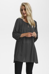 Tunique grise à manches longues avec un décolleté en trou de serrure, coupe ample et manches froncées. Tissu léger avec une texture douce. Associée à un pantalon noir.