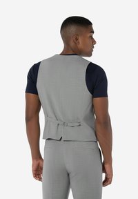 Graues Stoffwesten mit taillierter Form, ausgestattet mit einem Rückengurt zur Anpassung, kombiniert mit einem dunkelblauen kurzärmeligen Hemd. Geschmeidige Textur, maßgeschneiderter Look.