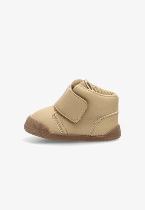 Zapato beige para bebé con correa de Velcro, suela marrón texturizada y cuello acolchado en el tobillo sobre un fondo blanco.