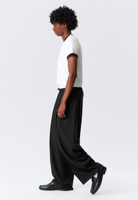 Camiseta blanca de manga corta con ribete negro, combinada con pantalones negros holgados y mocasines negros. Texturas simples y suaves con un corte relajado.