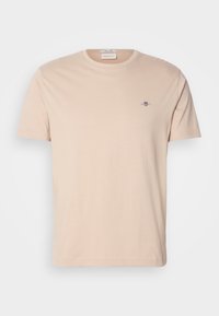 T-shirt beige à manches courtes et col rond avec petit logo brodé sur le côté gauche de la poitrine, présenté sur un fond uni.