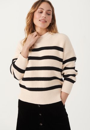 Maglione beige a righe con strisce nere, texture a costine e colletto alto. Indossato con una gonna di velluto a coste nera con bottoni frontali.