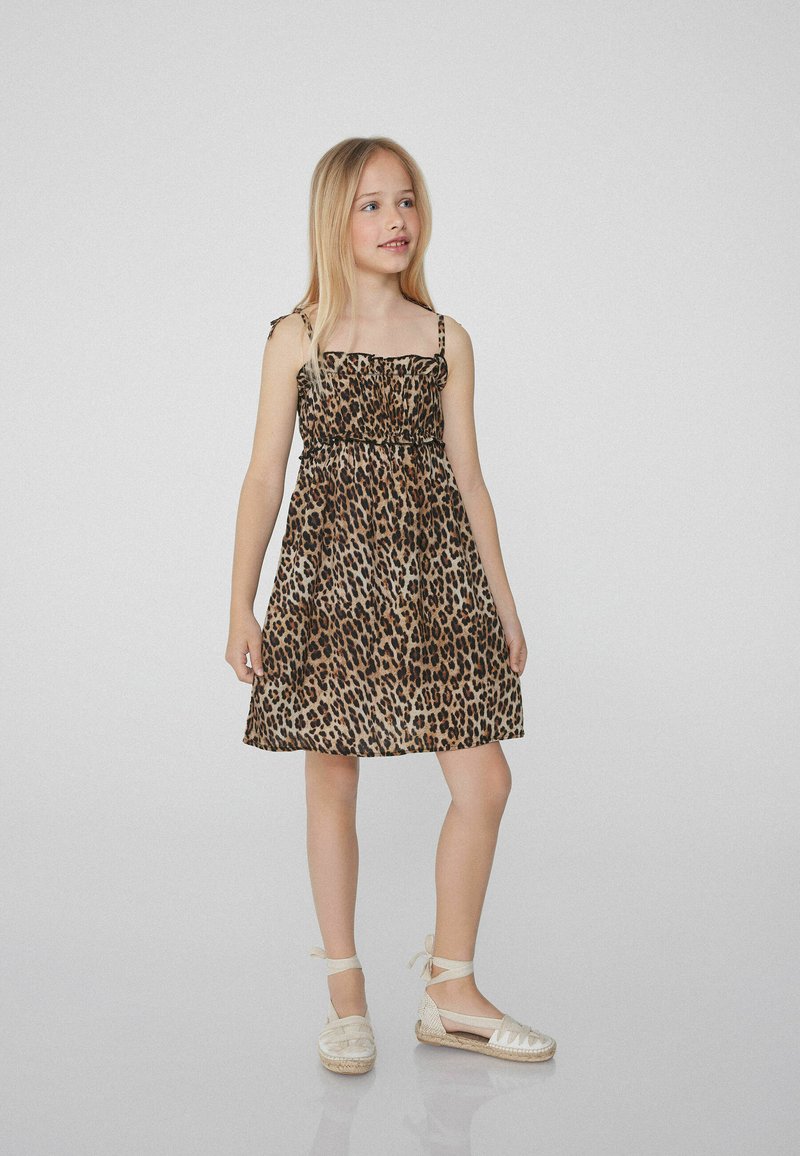 Robe en imprimé léopard avec fines bretelles et corsage froncé. Tissu doux, longueur genou, complétée par des chaussures espadrilles beiges.