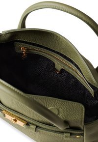 Interno di una borsa a tracolla in pelle verde testurizzata che mostra una tasca con zip dotata di accessori in oro e una fodera nera a motivo.