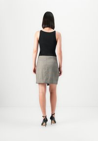 Svart ribbet tanktopp kombinert med et grått rutete miniskjørt, med en bakre glidelås og slisse. Modellen har på seg svarte høyhælte sko.