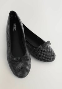 O pereche de balerini negri strălucitori cu fundițe mici pe vârfuri, tălpi moi și un design texturat subtil.