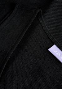 Κοντινό πλάνο μαύρου υφασμάτινου υλικού με διπλωμένες άκρες και μια μικρή λευκή ετικέτα που φαίνεται εν μέρει στη δεξιά πλευρά.