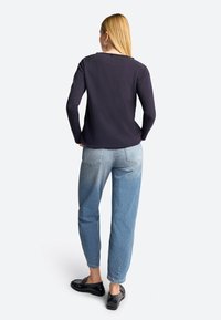 Maglia a maniche lunghe navy in tessuto morbido, abbinata a jeans tapered blu chiaro. Mocassini neri completano l'outfit. Vista posteriore mostrata.