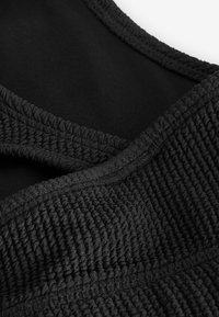 Tessuto nero testurizzato con una superficie rigata e aree lisce, creando un design a strati. Presenta un collo rotondo e materiali a contrasto.