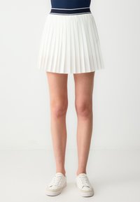 Witte plaaidrok met een aansluitende marineblauwe tailleband, voorzien van horizontale witte accenten. Lichtgewicht stof met een gladde textuur.