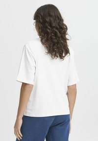T-shirt bianco in cotone con maniche corte, vestibilità rilassata e orlo dritto. La parte posteriore presenta una texture liscia senza motivi visibili.
