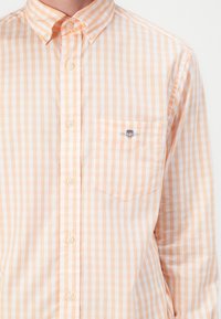 Camicia a maniche lunghe in leggero arancione e bianco a quadretti, con taschino sul petto e logo ricamato. Tessuto in misto cotone.