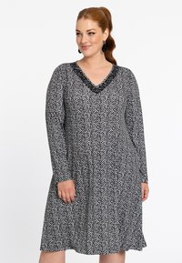 Robe à rayures en chevron noir et blanc avec manches longues, décolleté en V et détail texturé au niveau du col. Silhouette évasée, longueur genou.