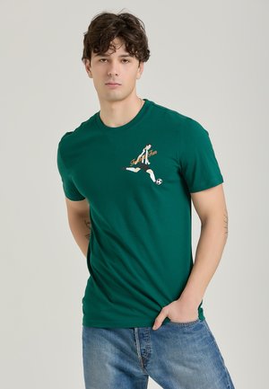 Grøn bomulds t-shirt med korte ærmer, der har et grafisk motiv af en fodboldspiller i bevægelse og teksten "Football Fun" i orange.