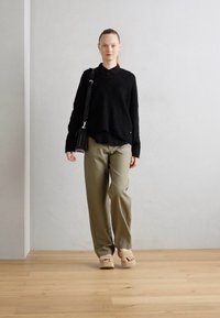 Crna pletena džemper sa ovratnikom, slobodnog kroja; maslinasto zelene hlače širokog kroja; bež cipele na slip-on; mala crna torba za rame.
