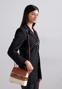 Tkanica torba iz košarice s smešnim kožnim detaljima, pravokutnog oblika, s kratkim ručkama, prikazana s crnim blazerom.