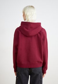 Μπορντό φούτερ με κουκούλα και κορδόνι, ραμφαλά μανίκια και στρίφωμα. Μαλακό, υφασμάτινο ύφασμα. Φοριέται με σκούρους παντελόνες πολλαπλών τσέπες.