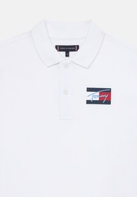 Witte polo shirt van katoen, voorzien van een klassieke kraag, drie knopen en een geborduurd Tommy Hilfiger logo in rood en blauw.