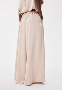 Pantalons larges en tissu beige doux, dotés d'une taille élastique, de poches latérales et d'une texture lisse. La coupe ample améliore le confort.