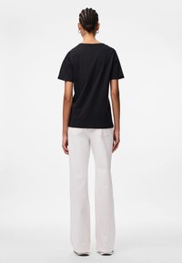 Camiseta de algodón negra de manga corta, vista desde la espalda, combinada con unos pantalones vaqueros acampanados de tiro alto y color claro. Textura suave.