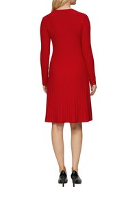 Rotes, geripptes Langarmkleid mit schwingendem Saum, runder Halslinie und taillierter Silhouette, kombiniert mit schwarzen High Heels.