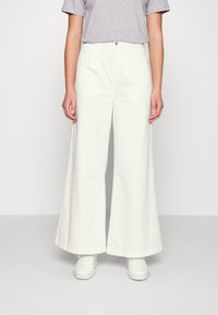 Jeans blancos de pernera ancha, fabricados en algodón con una textura suave, presentan una cintura alta, cierre frontal con botón y bolsillos laterales.
