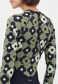 Langermet våtdrakt med blomstermønster i grønn, svart og hvit, med glidelås bak og en tettsittende design. Roxy-logoen nederst.